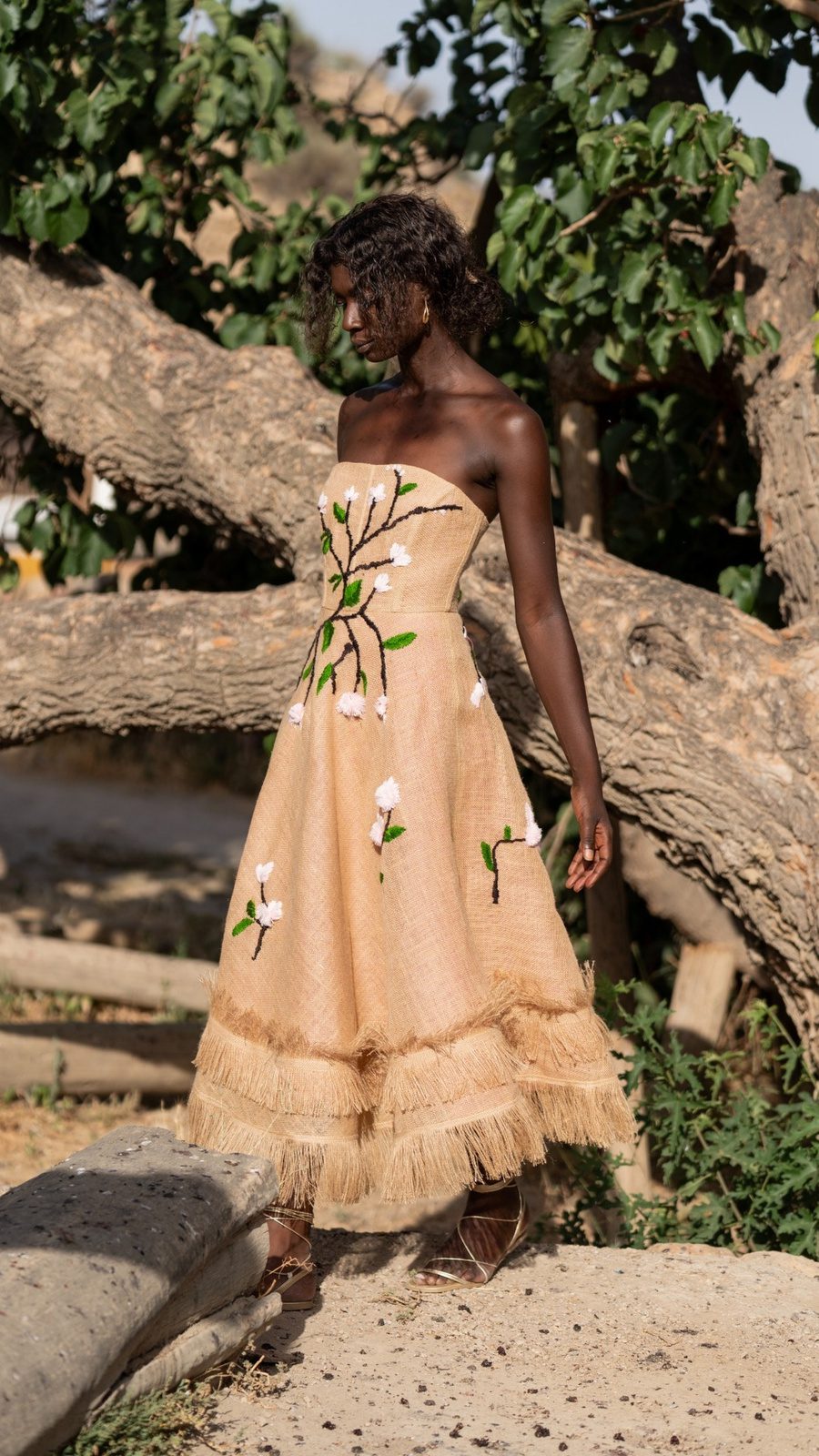 Modelo con vestido de arpillera, cuerpo palabra de honor, bordado floral y falda larga en A con flecos.