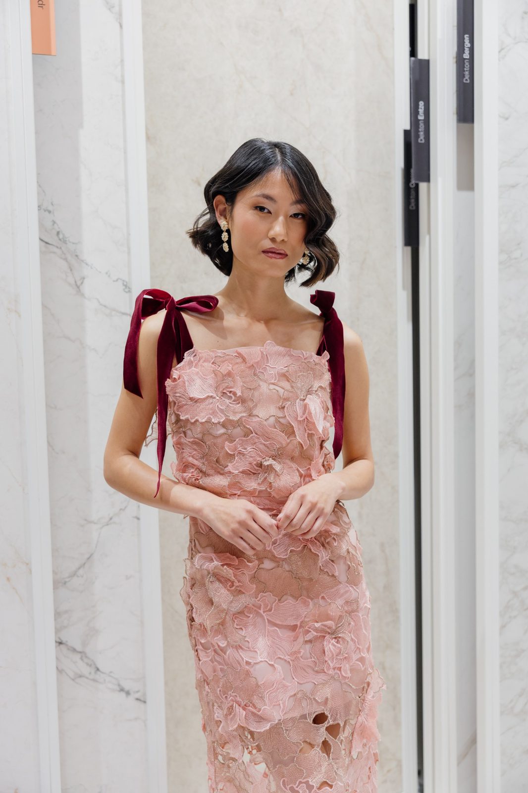 Mujer con vestido rosa de encaje y lazos de terciopelo burdeos anudados en los hombros.