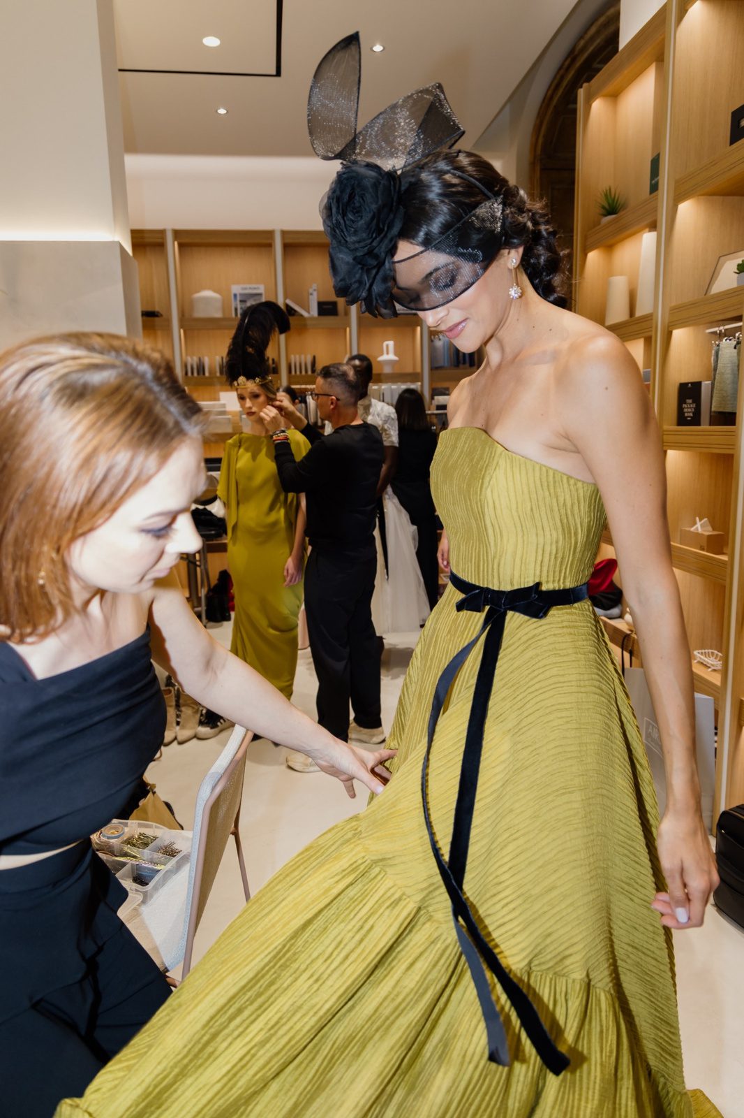 Mujer durante una prueba con vestido verde oliva palabra de honor, cintura marcada con lazo negro y falda amplia.